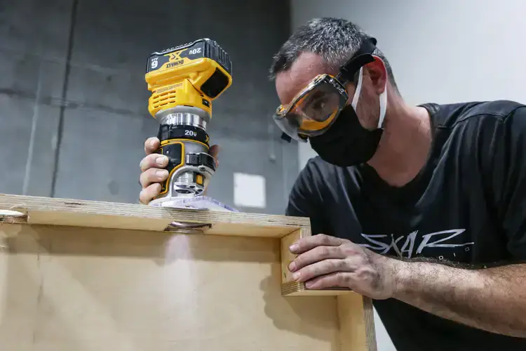 A guy holding a cordless router routing a hole in a speaker enclosure